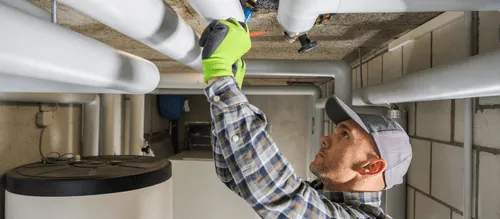   Licensed technician performing HVAC inspection on overhead piping in commercial facility